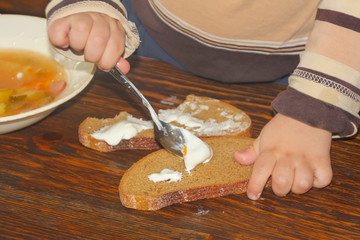 A child smears sour cream on bread. spread the cream on a roll. Children learn to spread a spoonful of sour cream.