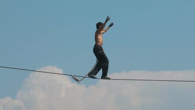 The tightrope Walker is on the rope stretched high in the mountains. Against the sky.
