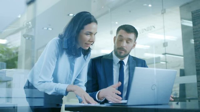 Beautiful Female Manager Gives Advice to a Businessman sitting at His Desk. They Do High-Five. Working on a Laptop in Modern Office. Shot on RED EPIC-W 8K Helium Cinema Camera.
