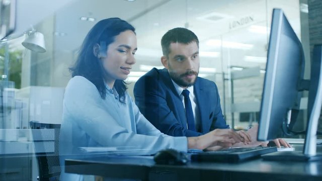 Female Accountant and Male Businessman Sitting at the Desk Having Discussion and Working on a Desktop Computer, Solving Problems. Shot on RED EPIC-W 8K Helium Cinema Camera.