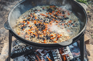 Cooking pilaf in a large cauldron with a strong steaming on an open fire outdoors on a Sunny summer...