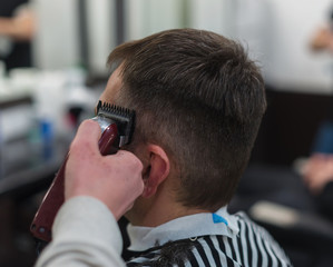 The hands of young barber making haircut to attractive man in barbershop