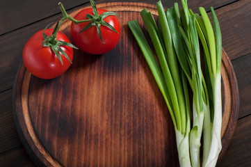Natural products vegetables tomatoes and green onions on an old kitchen board.
