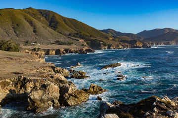 Fototapeta na wymiar Dramatic landscape view of a Big Sur road trip on a sunny day with waves crushing .