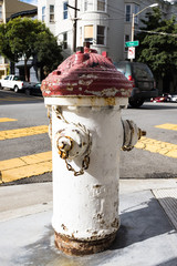 An old vintage fire water hydrant painted white and red on the corner of the street, casting a shadow on a sunny day