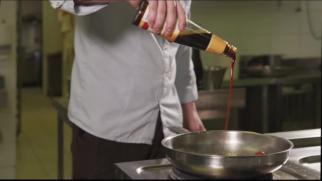 close up shot of the man's hands, the chef uses soy sauce to prepare a vegetable dish, he fries a bowl of leek, onions, tomatoes and pepper on a frying pan
