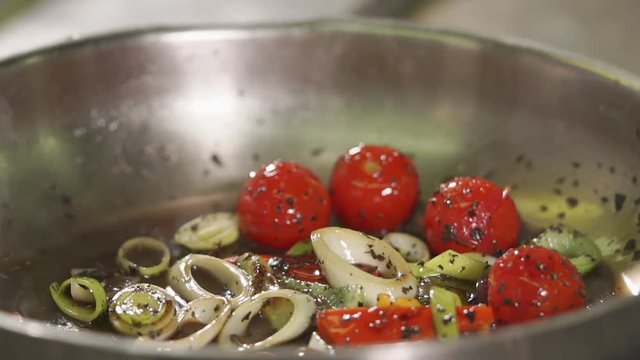 close up shot of a frying pan in which roasted in oil and spices tomatoes, onions and peppers, the chef shakes the frying pan and vegetables move on the dishes