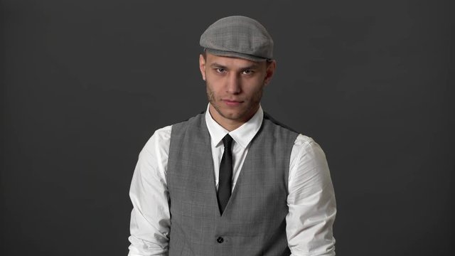Portrait of handsome mature guy in suit and peaky kepi shaking head in rejection meaning no, over gray wall. Concept of emotions