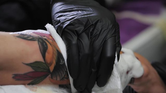 the final stage of the tattooing session. removal of foam antiseptic from fresh colorful trendy tattoo on the hand of young man. Slow motion.