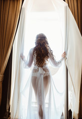 Fototapety  Silhouette of sexy young brunette woman in white lingerie in the doorway opening curtains