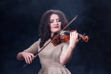 Close-up. Beautiful girl with dark hair on a smoky background. Violin and bow in female musical hands. Beautiful girl with dark hair on a smoky background.