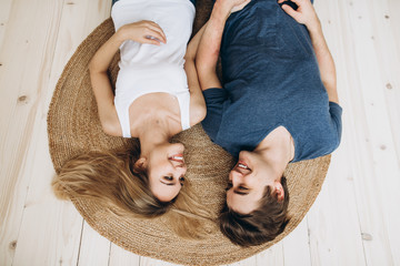 Happy loving couple lying on the floor on a small rug looking at each other and smiling. Top view