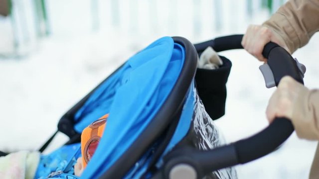closeup mother hands holding handle strolling baby blue carriage outside winter city walking day motherhood little boy unrecognisable childhood stroller buggy walk transport comfort modern lifestyle