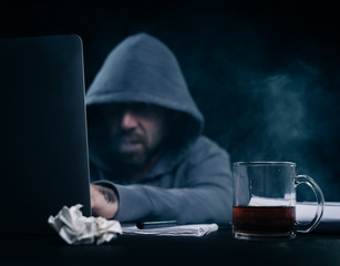 mysterious criminal male hacker, hides his face under the hood, doing something illegal on the...