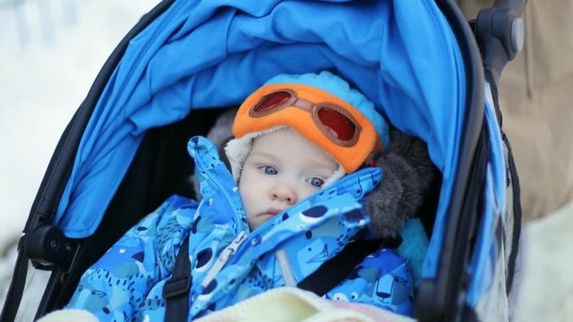 portrait sweet calm cute 9 months old baby boy beautiful huge blue eyes buggy outdoors winter walking carriage childhood chubby cheeks stylish pilot funny cap looking camera stroller child infant