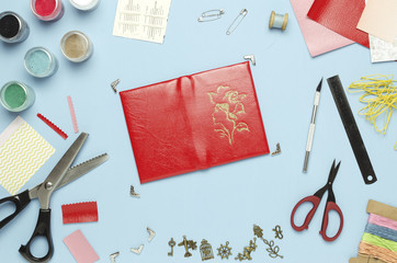 Bright red leather cover on a blue background with tools and materials. The view from the top