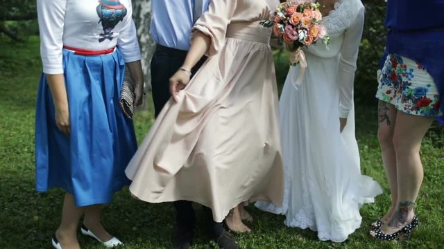 Bride and bridesmaid are holding bouquets of flowers in hands. Bridesmaid are on background.