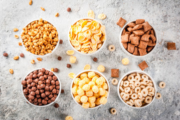 Set of various breakfast cereal corn flakes, puffs, pops, grey stone table copy space top view