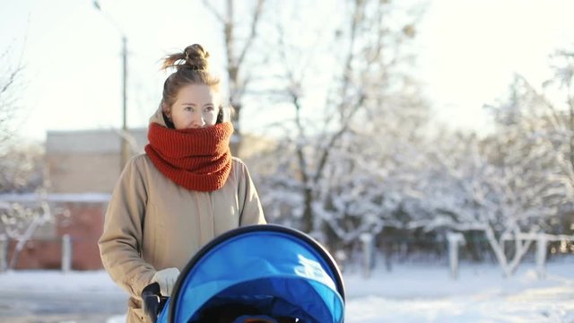young mother walk blue stroller baby carriage winter city snow park happy motherhood momy child love cute boy beautiful sunny day maternity parenting stylish mom toddler warm clothing leisure relax