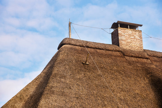 lightning rod on a thatched roof with a chimney against a blue sky with clouds, copy space