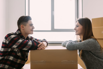 Young happy couple moving house looking each other leaning on a box