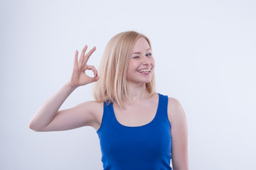 Woman makes ok, good sign with her hand and beaming. Beautiful blonde girl in blue shirt smiling and beaming