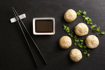 Fototapeta na wymiar Slate plate with tasty baozi dumplings and soy sauce, top view