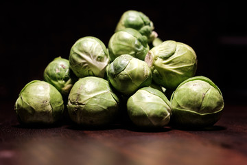 Fototapeta na wymiar raw green brussels sprouts heap on brown wooden surface - spot light - close up - untouched