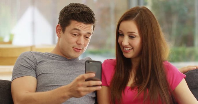 4K Cute young couple relaxing at home, talking & looking at smartphone. Slow motion