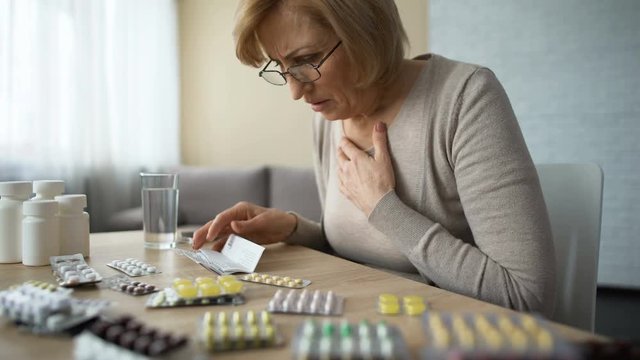 Sad woman looking at table full of pills and sighs, old age disease, addiction