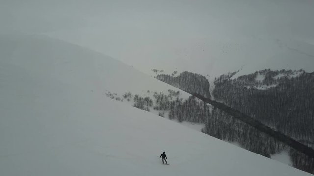 Aerial shot of Snowboarder descending by a mountain ridge. Birds Eye View Above White Powder Snow - Winter Extreme Sports, Freeride.