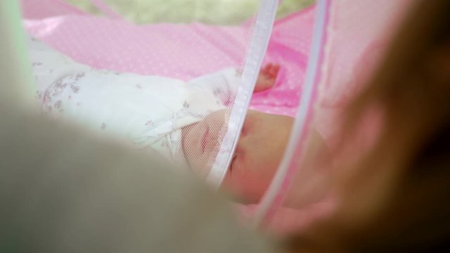 Mother opening portable pink bassinet with baby and taking daughters hand. Mom and child outdoor on summer day