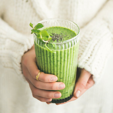 Matcha green vegan smoothie with chia seeds and mint in glass in hands of female wearing white sweater, square crop. Clean eating, detox, alkaline diet, weight loss concept