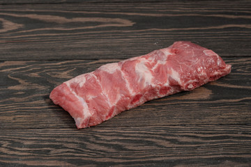 Fresh raw whole rack of pork loin with ribs on a dark background.