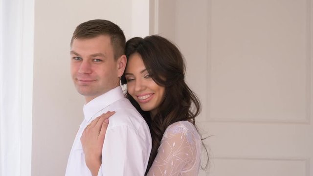 young couple in background white wall man in a suit girl with brakits in a tender serene dress will smile into the camera and smile in an embrace.