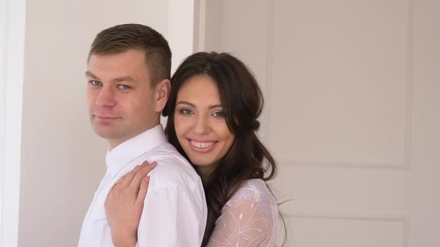 young couple in background white wall man in a suit girl with brakits in a tender serene dress will smile into the camera and smile in an embrace.