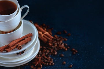 Close-up of a pile of dishes and cups with coffee beans and cinnamon on a dark blue background. Creative barista concept with copy space.
