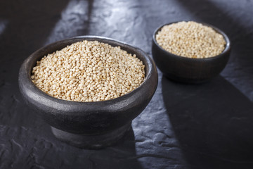 Quinoa grains with spoon and bowl on black background