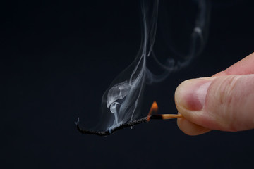 Burning and Smoking wooden match in hand on dark background.