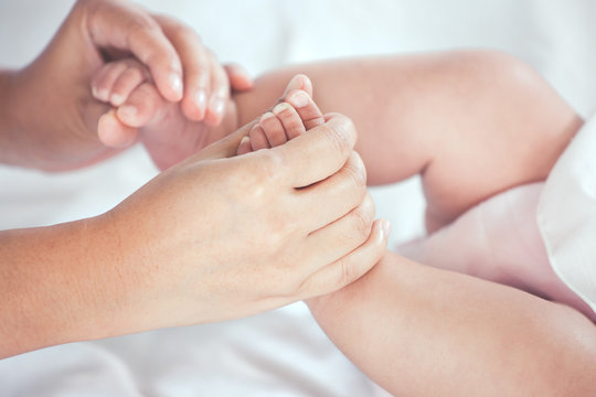 Mother hand holding little baby girl feet while she lying on bed with love and tenderness