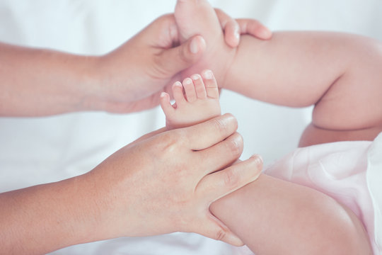 Mother hand holding little baby girl feet while she lying on bed with love and tenderness
