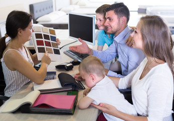 Obraz premium Smiling seller female is showing to young family the patterns of mattress fabrics