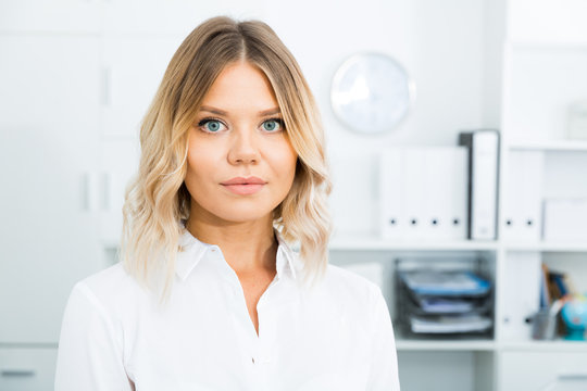 Blonde woman in corporate-type clothes in well-lit office close-up