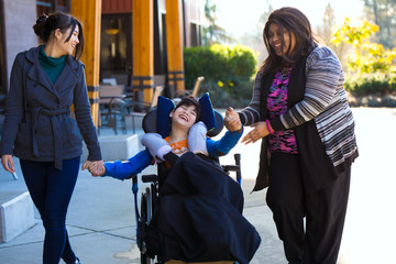 Disabled boy in wheelchair holding hands with caregivers on walk - Powered by Adobe