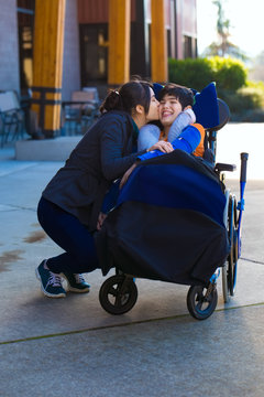Older sister kissing little disabled brother in wheelchair outdoors