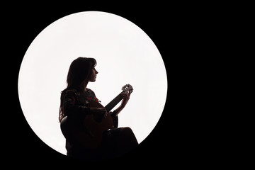 Silhouette of a beautiful brunette girl playing guitar. Concept for music news. Copy space. White circle as the moon on a black background.