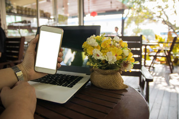 Woman hold smart phone empty screen over laptop in coffee cafe, business technology, mock up