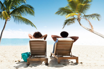 Couple relaxing on deck chairs at beach resort - Powered by Adobe