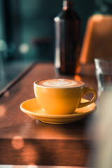 Flat white coffee in yellow cup on a wooden table at the hipster coffee shop. Latte art concept. Dark food photo. Vintage color filter effect. Copyspace , vertical