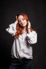 Portrait of a beautiful girl with long red hair in a white man's shirt on a dark background in the studio